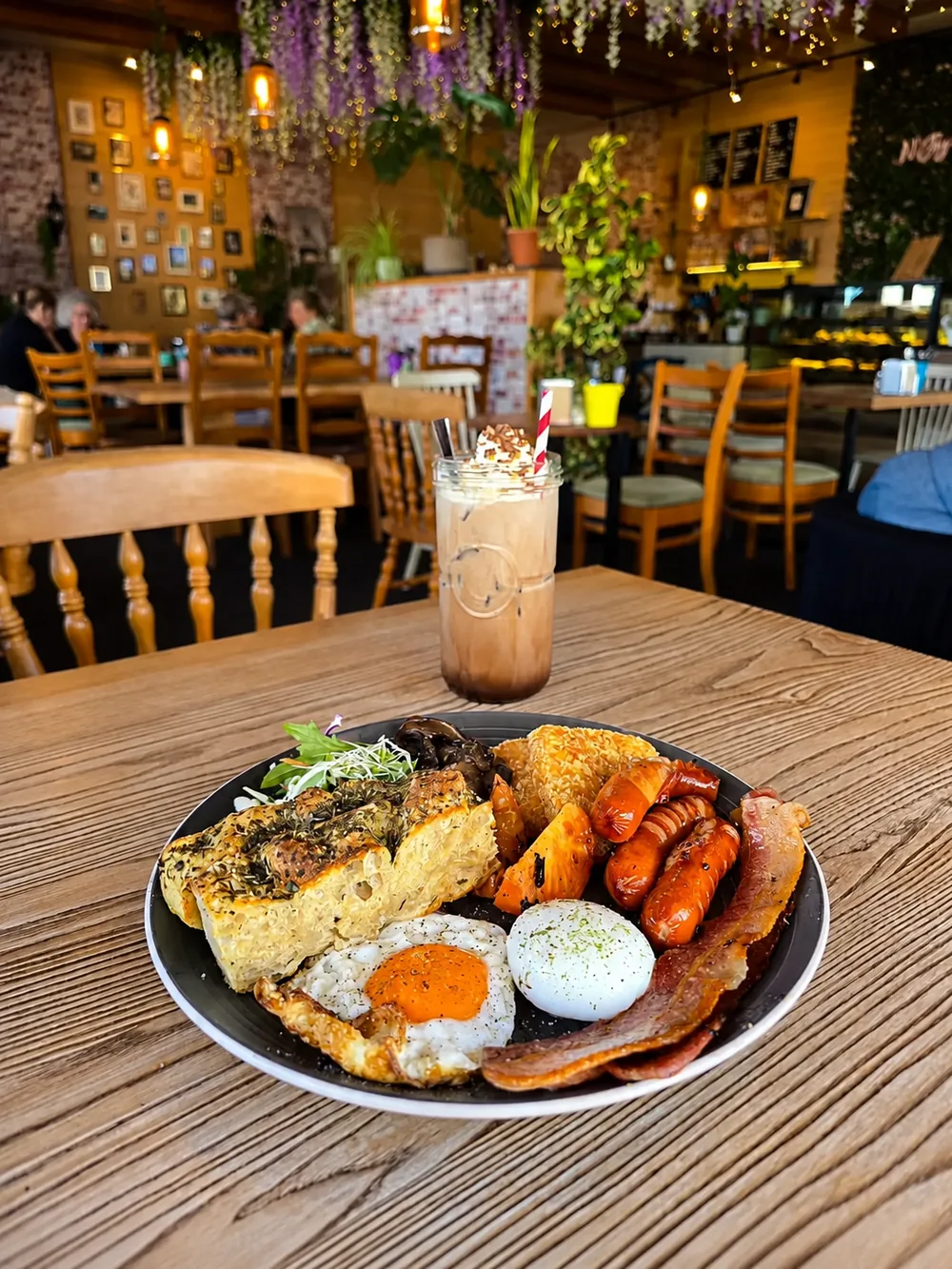 A big breakfast with eggs, toast, sausages and a hash brown, with hanging flowers behind